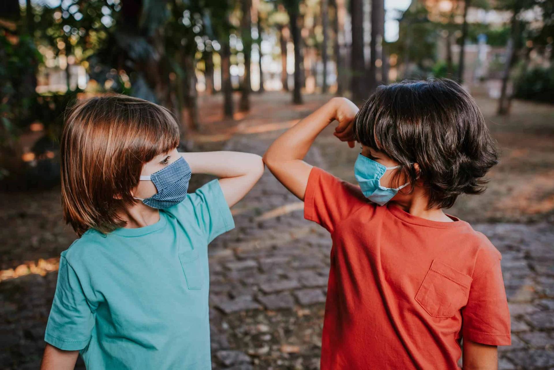 Deux enfants portant un masque se saluent du coude.
