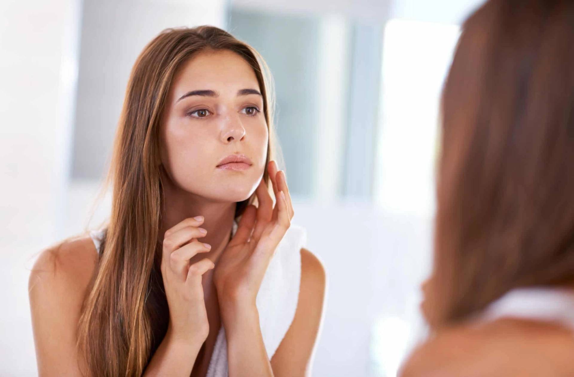 Une femme observe la peau de son visage dans un miroir.