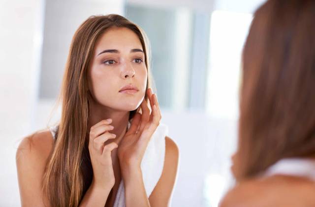 Une femme observe la peau de son visage dans un miroir.