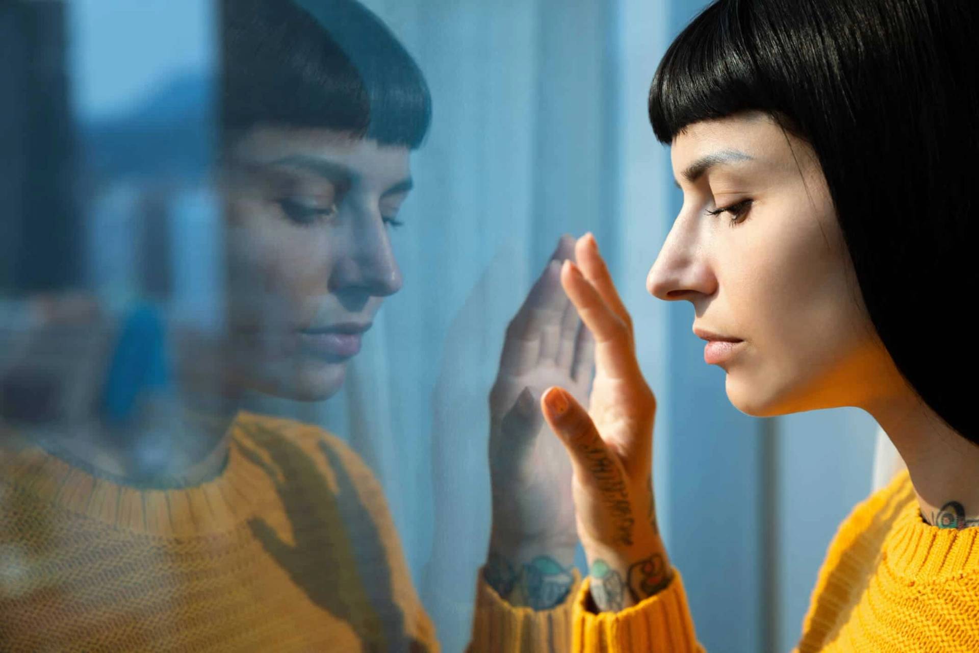 Une femme regarde à travers une fenêtre, une main posée sur la vitre.
