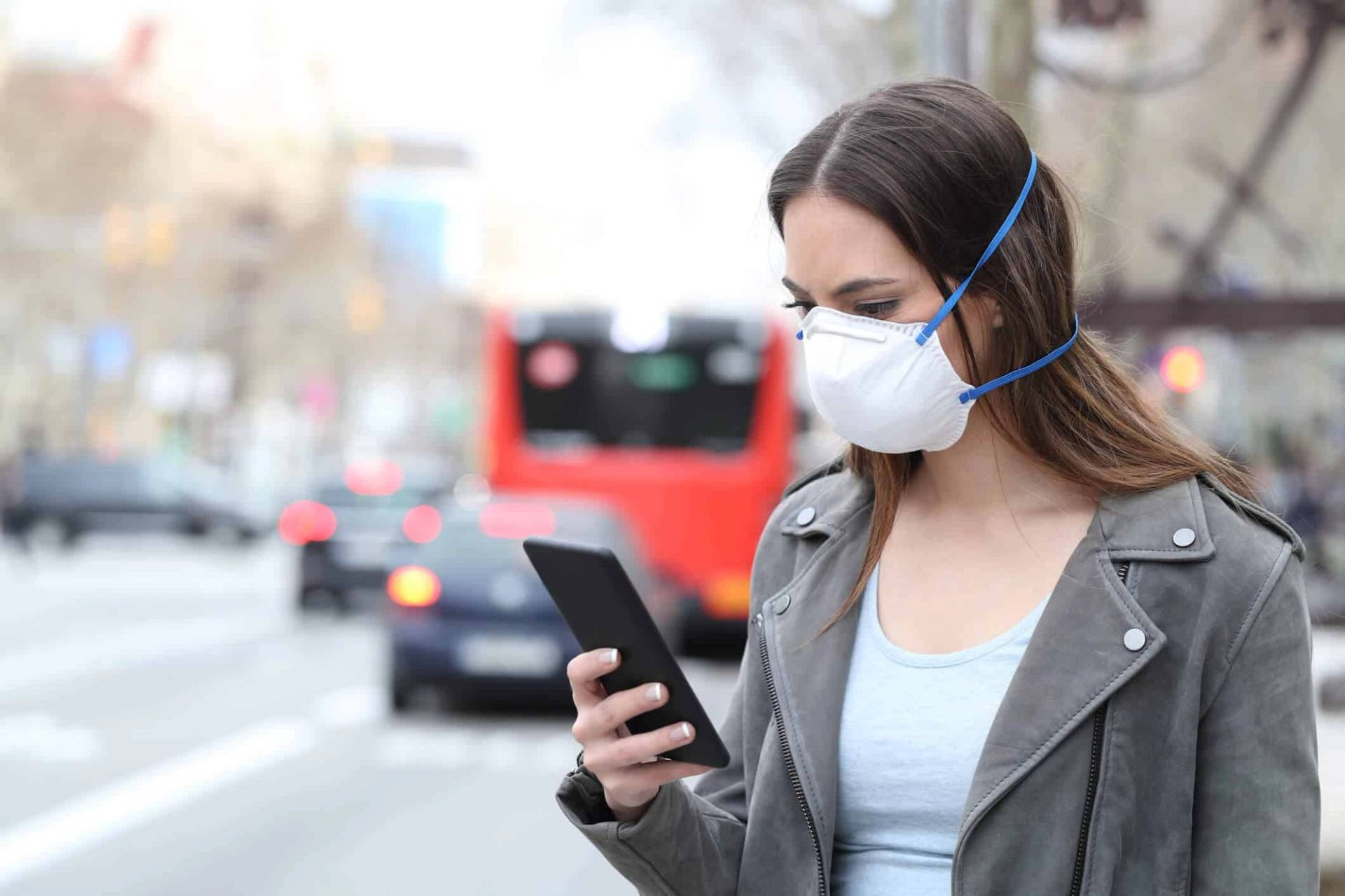 Une femme portant un masque consulte son téléphone dans la rue.