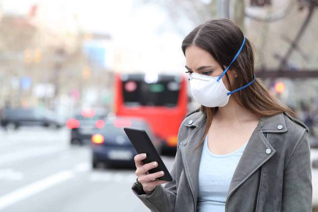 Une femme portant un masque consulte son téléphone dans la rue.