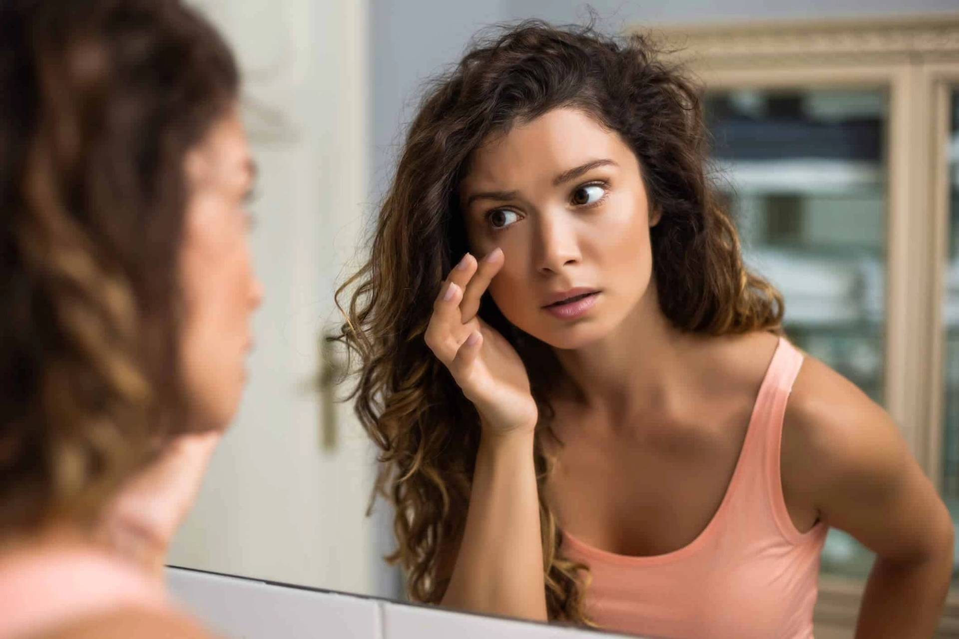 Une femme examine sa paupière dans un miroir.