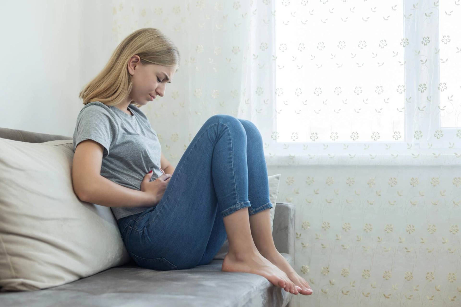 Une femme assise près d'une fenêtre pose une main sur son ventre.
