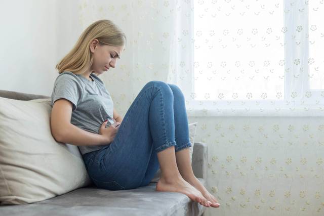 Une femme assise près d'une fenêtre pose une main sur son ventre.