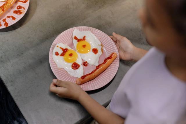 Enfant tenant une assiette où des œufs et une saucisse forment un visage.