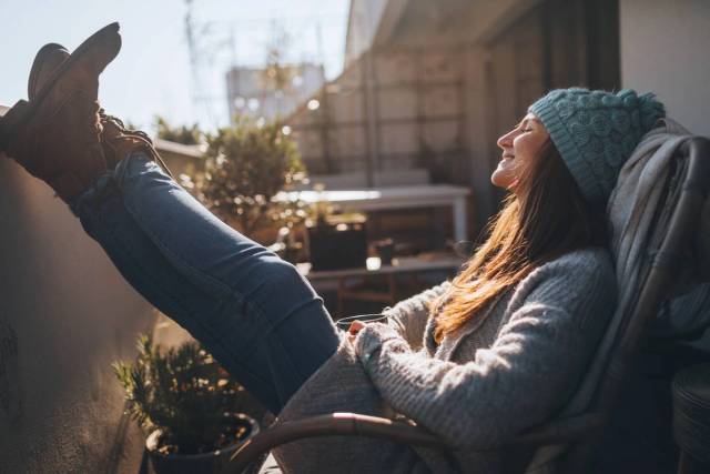 Femme en bonnet assise sur un balcon, les pieds relevés.