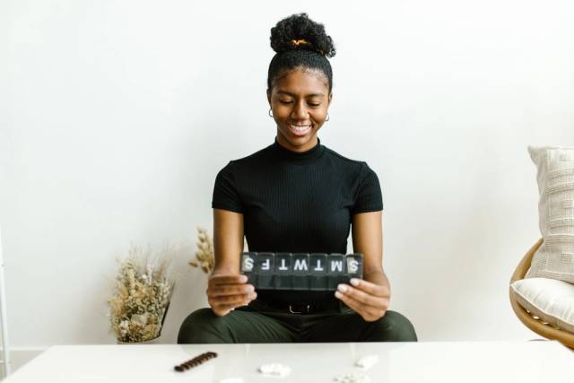 Femme noire souriante tenant un contenant de pilules hebdomadaire, promouvant la sensibilisation à la santé