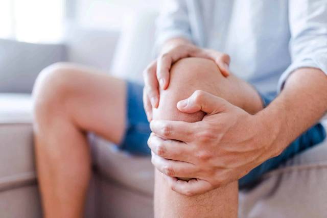 Une personne assise serre son genou avec les deux mains.
