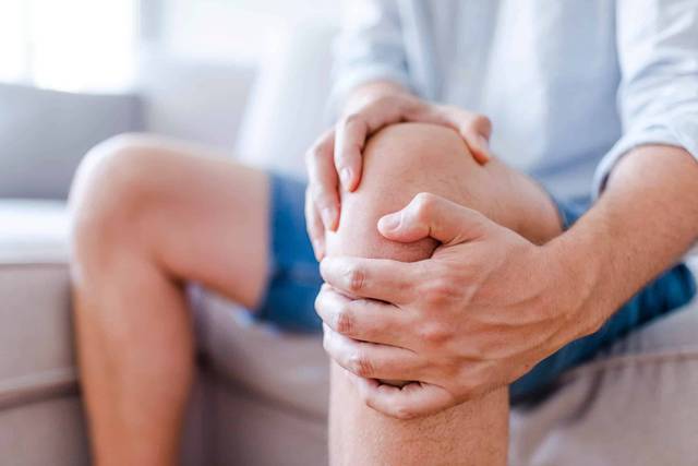 Une personne assise serre son genou avec les deux mains.