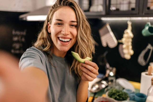 Une femme sourit en tenant une branche de céleri dans sa cuisine.
