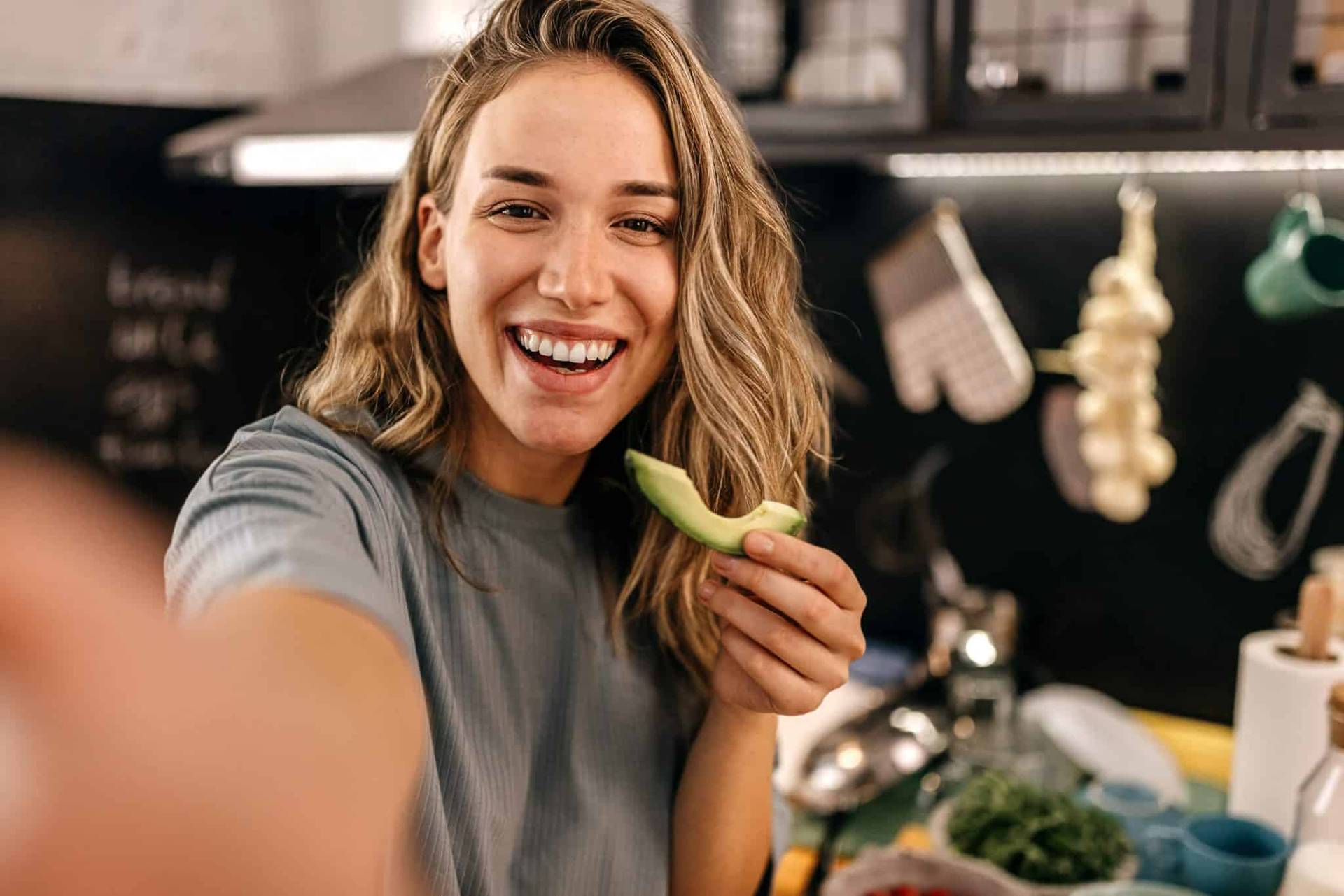 Une femme sourit en tenant une branche de céleri dans sa cuisine.