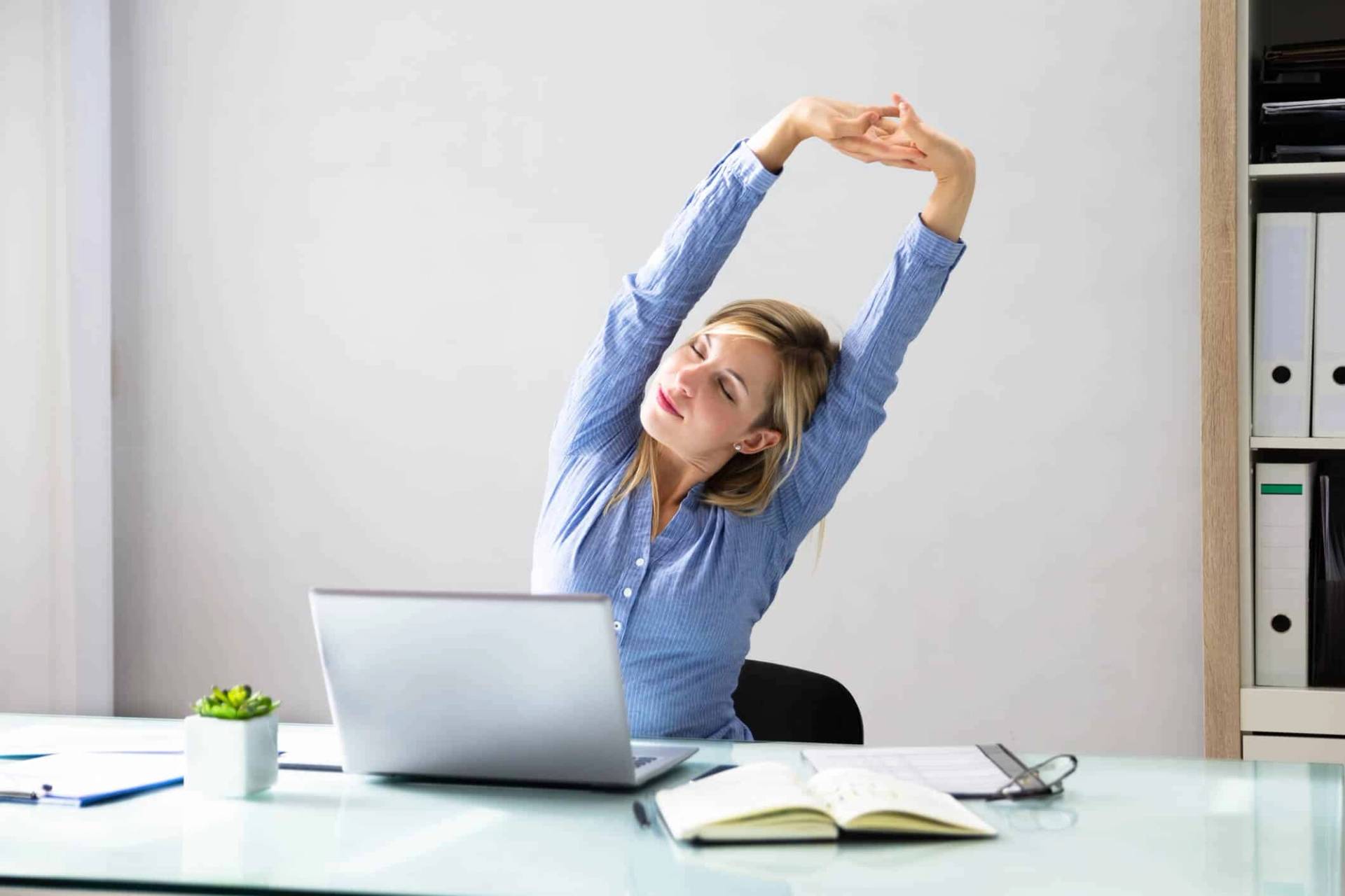 Femme qui s’étire à son bureau, devant un ordinateur portable.