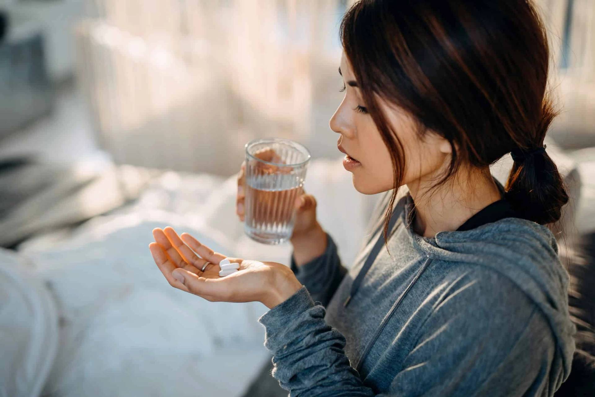 Une femme tient des comprimés et un verre d'eau.