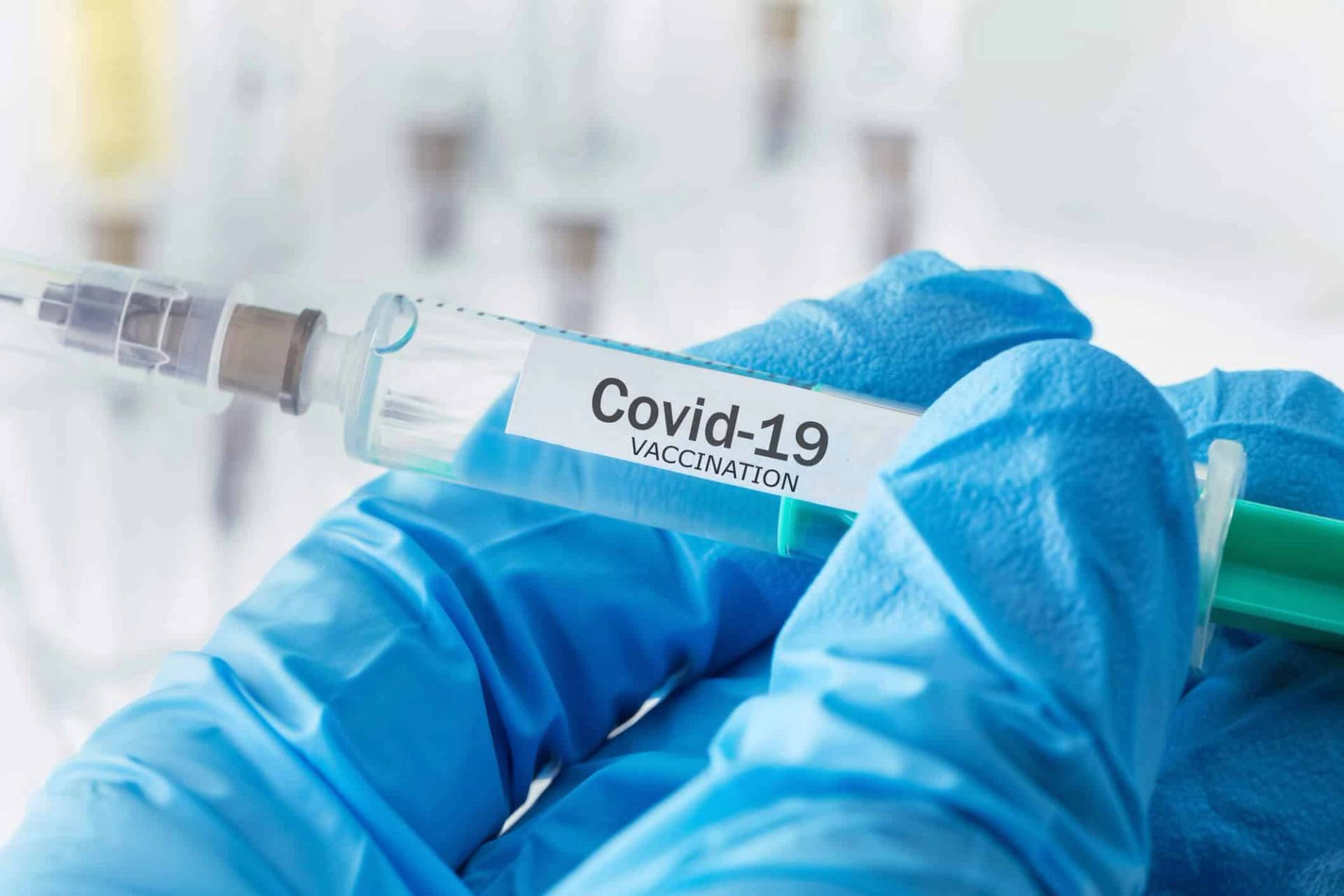 Des mains gantées tiennent une seringue portant une étiquette Covid-19.