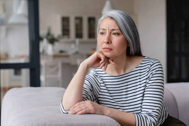 Une femme aux cheveux gris est assise à une table, le menton posé sur sa main.