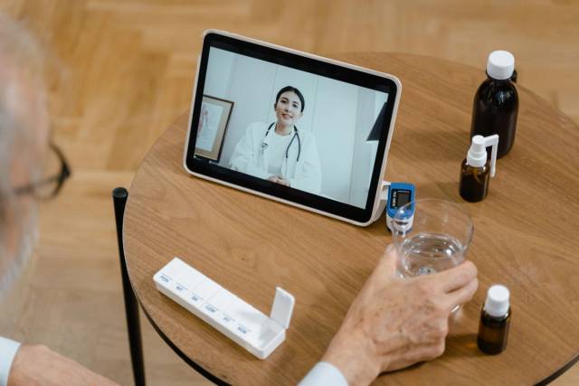 Un senior ayant une consultation virtuelle avec un médecin sur une tablette, avec des médicaments sur la table