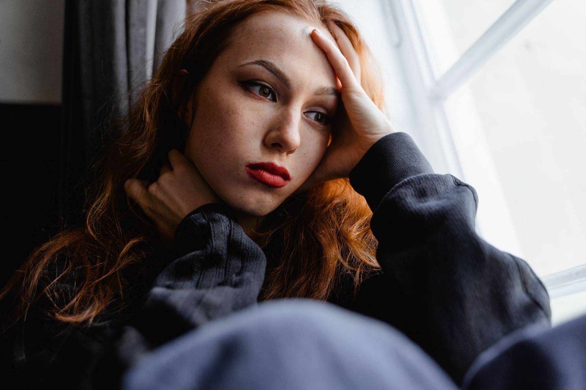 Une jeune femme avec une expression pensive regarde par la fenêtre dans un moment d'introspection