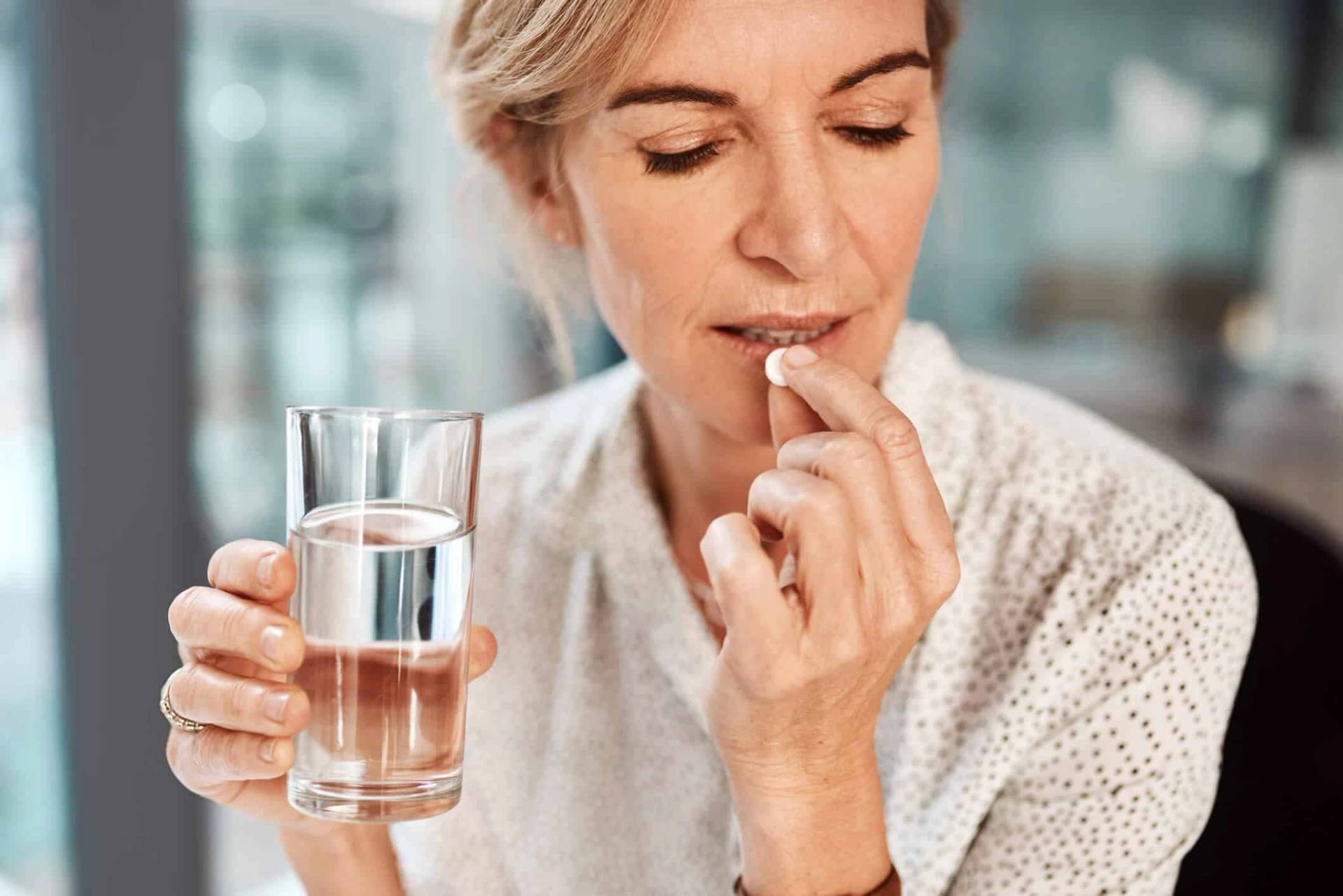 Une femme prend un comprimé avec un verre d'eau.