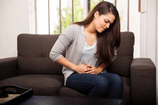 Une femme assise sur un canapé se tient le ventre.