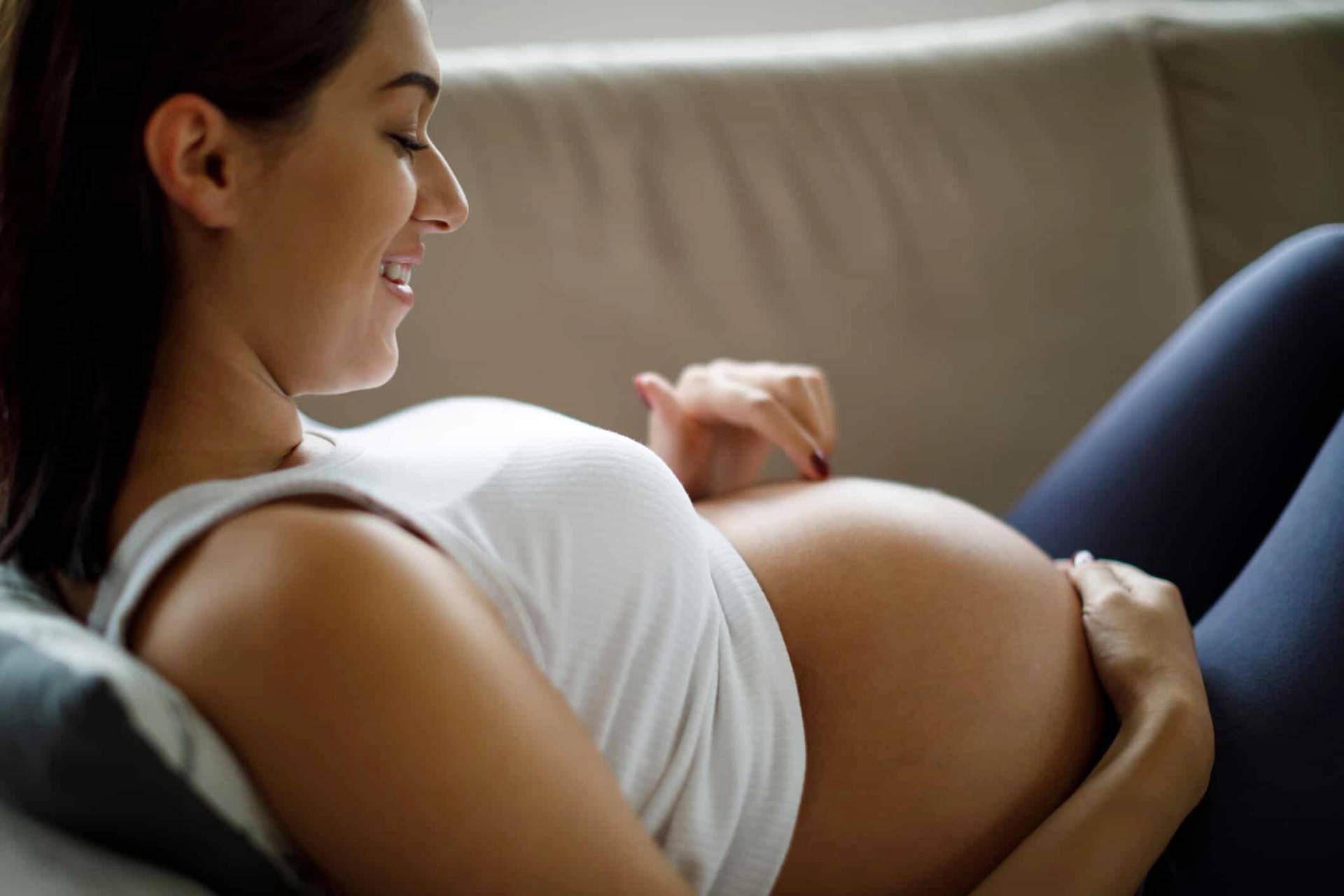 Une femme enceinte allongée sourit en regardant son ventre.