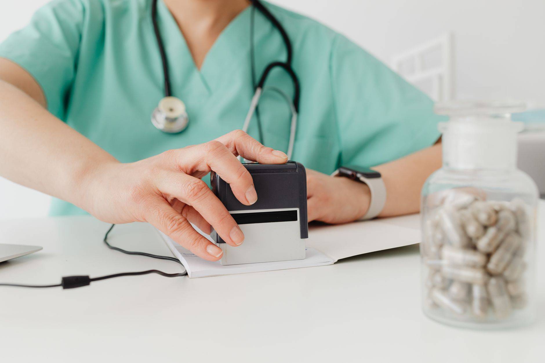 Gros plan d'un médecin tamponnant une ordonnance avec un flacon de pilules sur un bureau