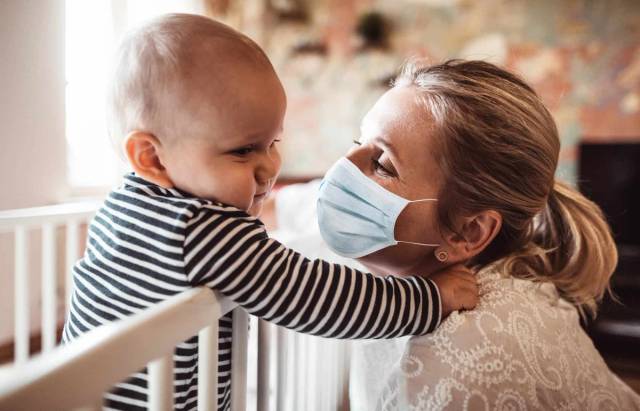 Une femme portant un masque tient un bébé dans ses bras.