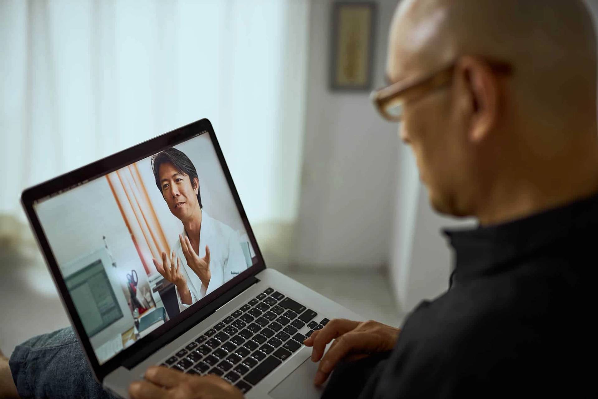 Un homme échange avec une médecin en vidéo sur un ordinateur.