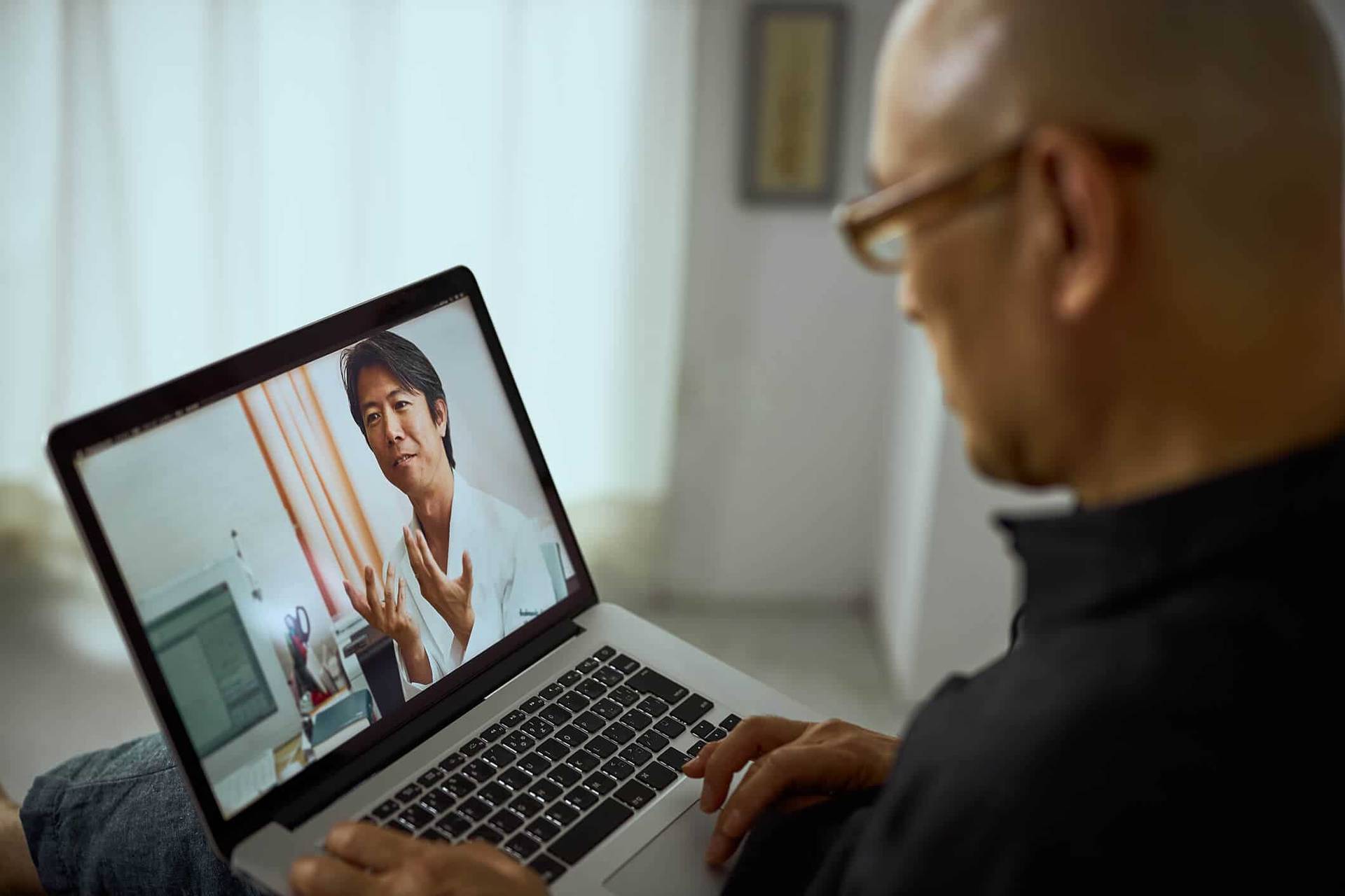 Un homme échange avec une médecin en vidéo sur un ordinateur.
