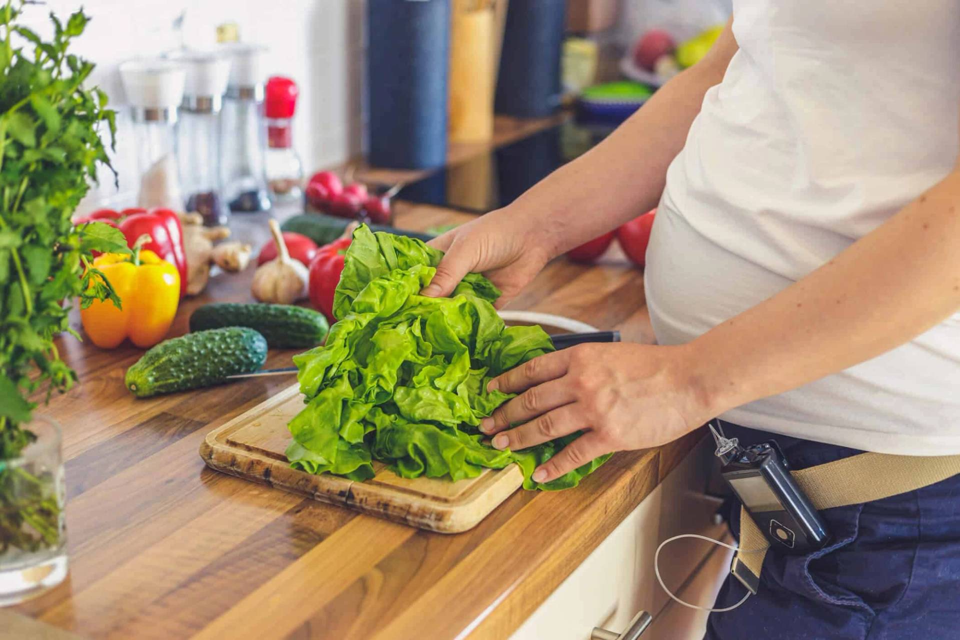 Une femme enceinte coupe des légumes dans sa cuisine.