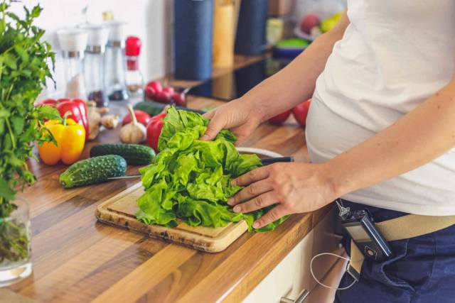 Une femme enceinte coupe des légumes dans sa cuisine.