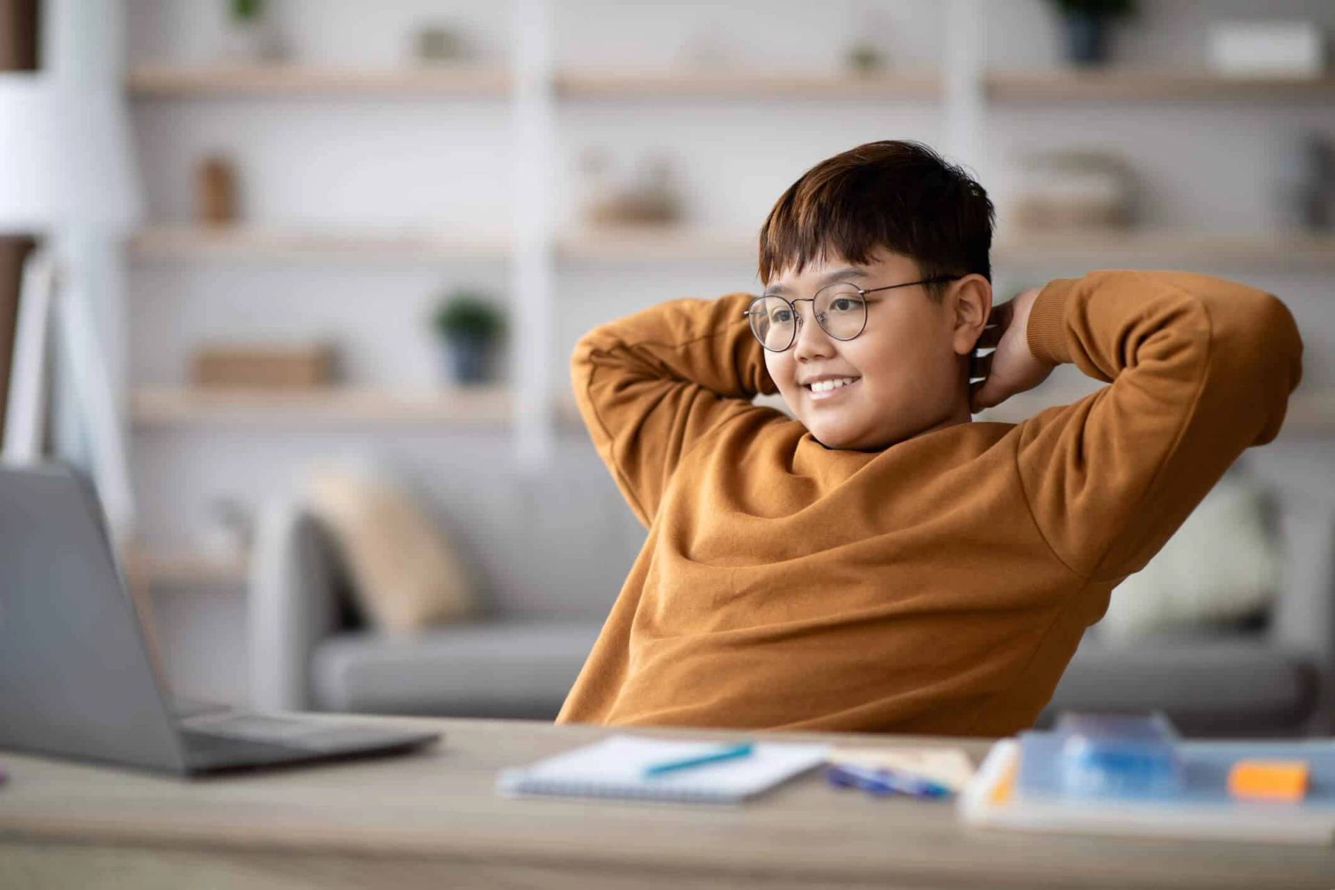 Un enfant se détend devant un ordinateur, les mains derrière la tête.