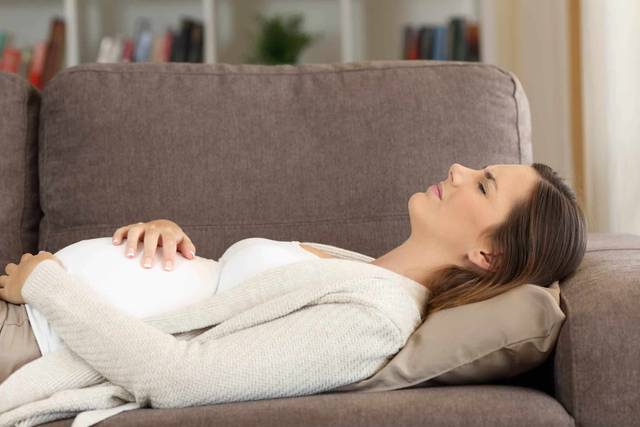 Une femme enceinte est allongée sur un canapé, les mains sur le ventre.