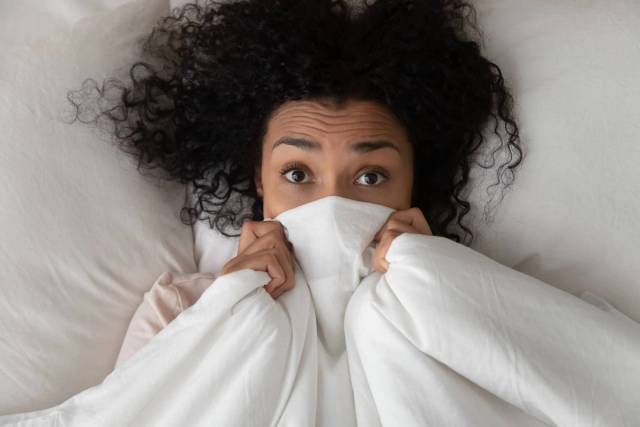 Une femme dans son lit remonte la couverture jusqu'à son visage.