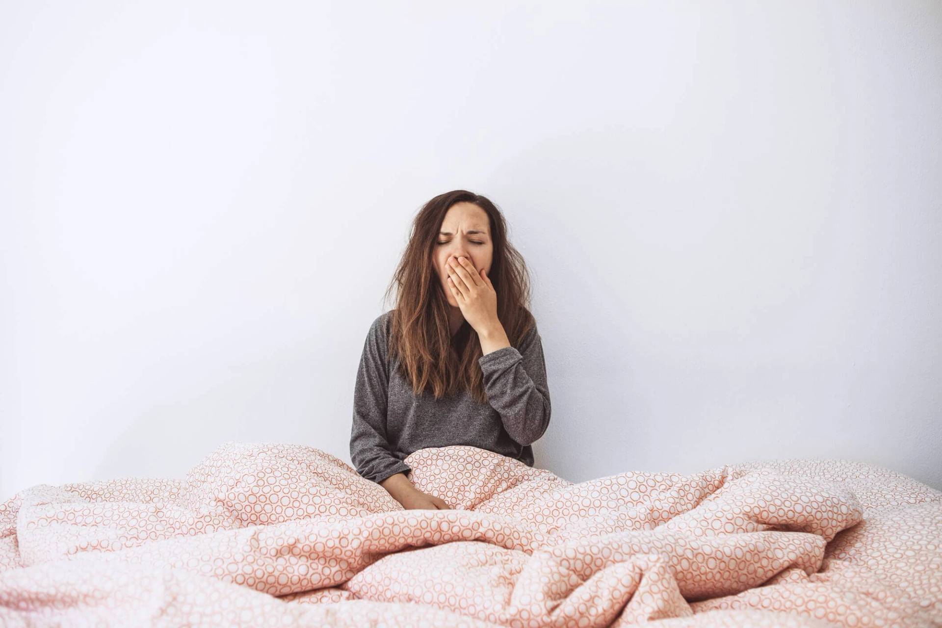 Une femme assise dans son lit bâille.