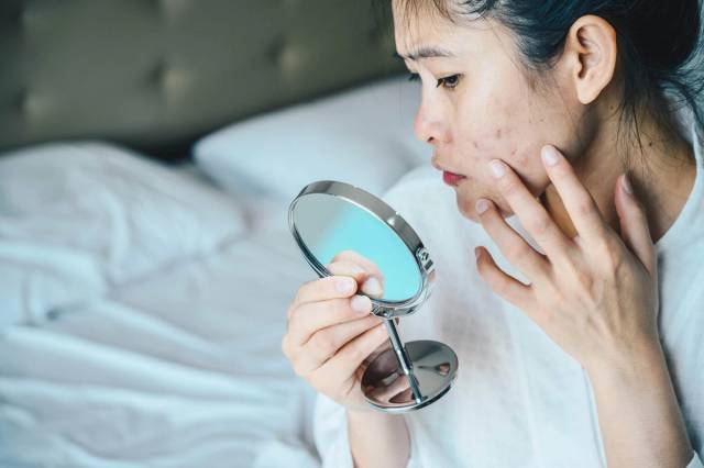 Une femme examine les boutons de son visage dans un miroir à main.