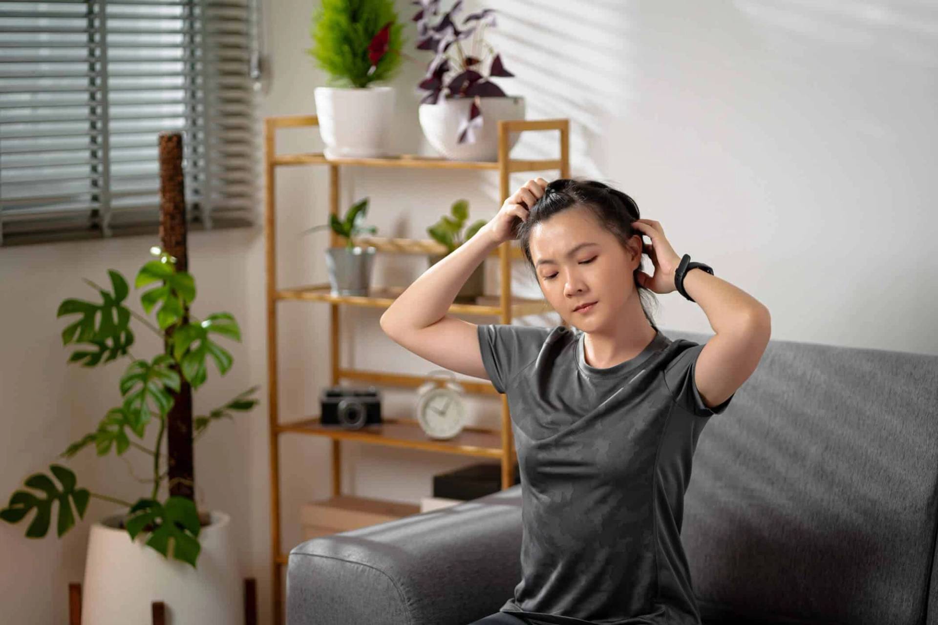 Femme assise sur un canapé, mains dans ses cheveux.