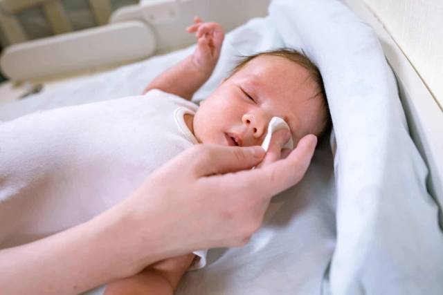Un adulte nettoie délicatement le contour de l’œil d’un bébé avec un coton.