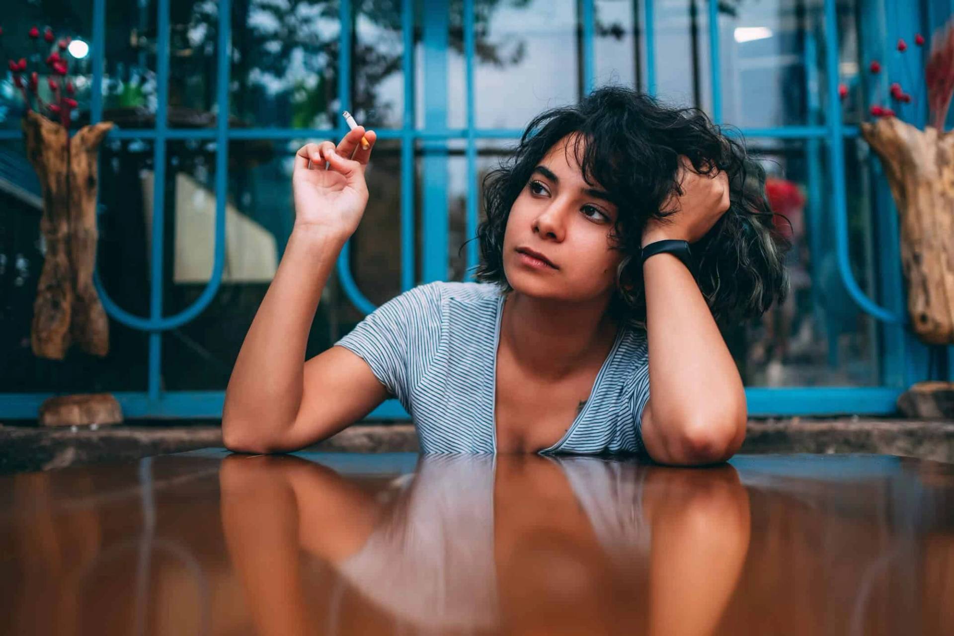 Femme assise à une table, une cigarette à la main.