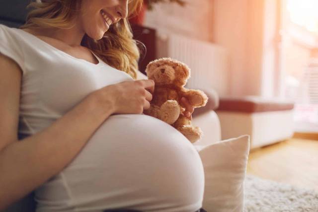 Femme enceinte tenant un ours en peluche contre son ventre.
