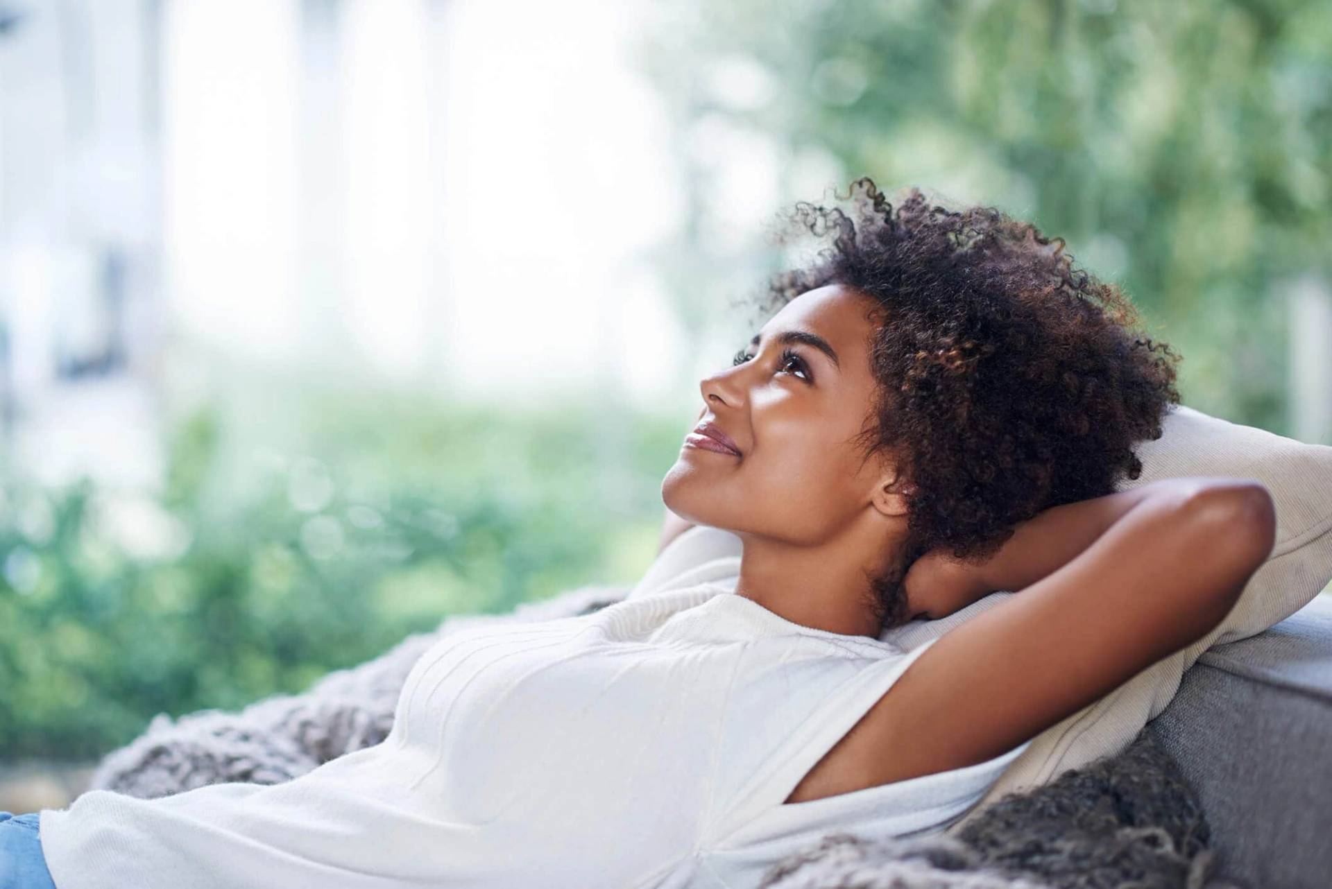 Femme allongée, souriante, près d’une fenêtre.