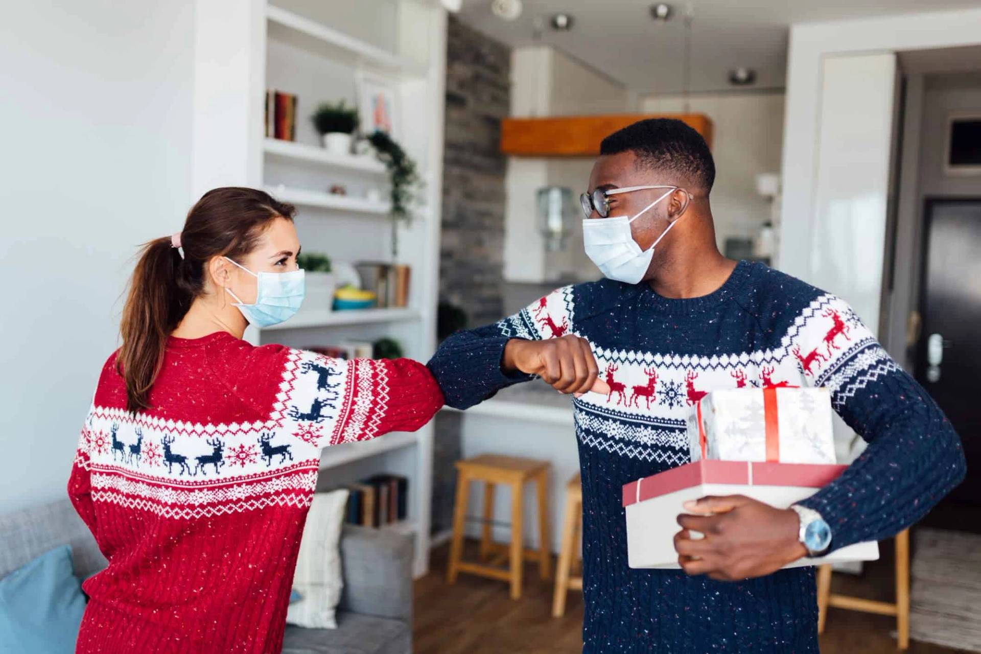 Deux personnes masquées en pulls de Noël se saluent avec le coude.