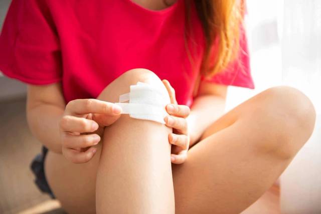 Femme posant un pansement sur son genou.