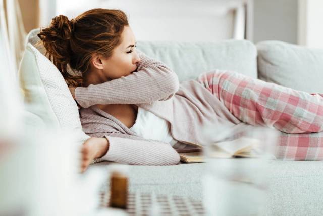 Femme allongée sur un canapé et toussant dans son coude.