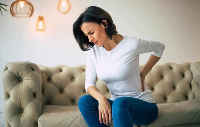 Femme assise sur un canapé, main sur le bas du dos.