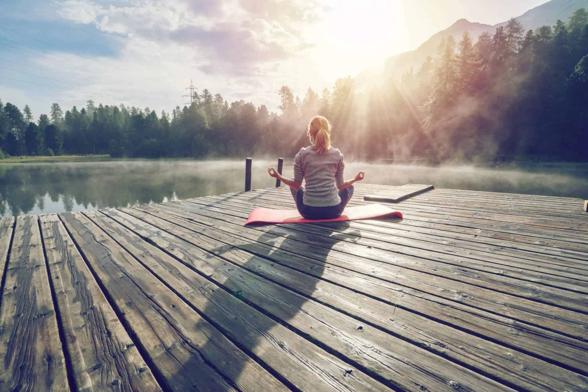 Personne assise en méditation sur un ponton près d’un lac.