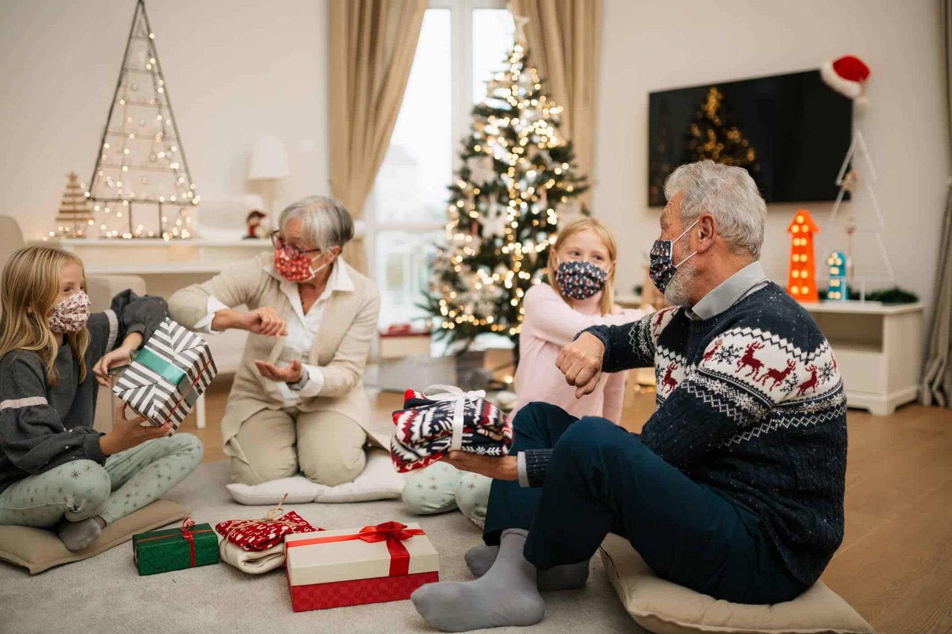 Groupe portant des masques et ouvrant des cadeaux près d’un sapin.