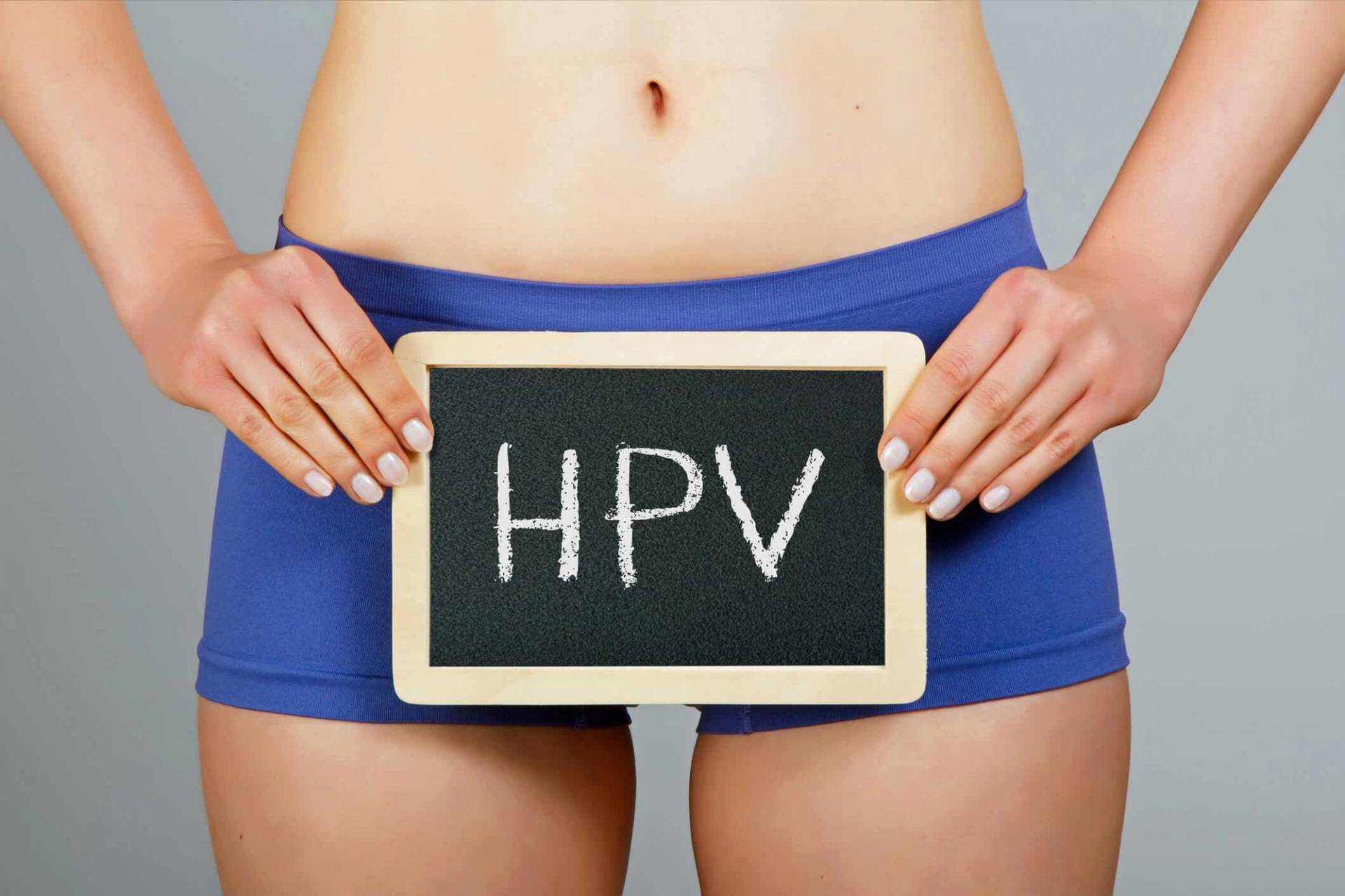 Femme en short bleu tenant une pancarte avec les ininitiales HPV pour le mot papillomavirus en anglais.