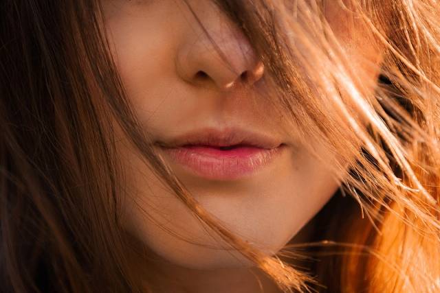 Gros plan artistique des lèvres d'une femme partiellement couvertes par des cheveux illuminés par le soleil