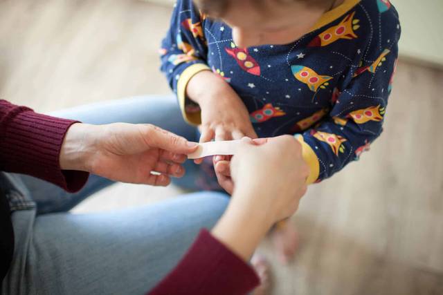 Adulte posant un pansement sur le doigt d’une enfant.
